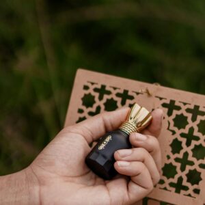 Close-up of a hand holding a black perfume bottle with a gold cap, showcasing elegance.